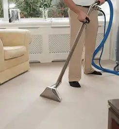 Professional carpet cleaner using a hot-water extraction wand and hose machine in a living room in South Bend, IN.