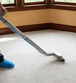 Steam carpet cleaning technician using a hot-water extraction wand on a residential carpet, wearing blue protective shoe covers South Bend, IN.