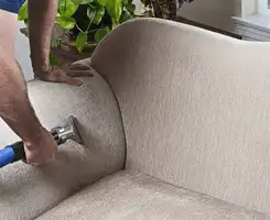 Professional upholstery cleaner deep-cleaning a fabric sofa with a handheld extraction tool and hose in South Bend, IN.